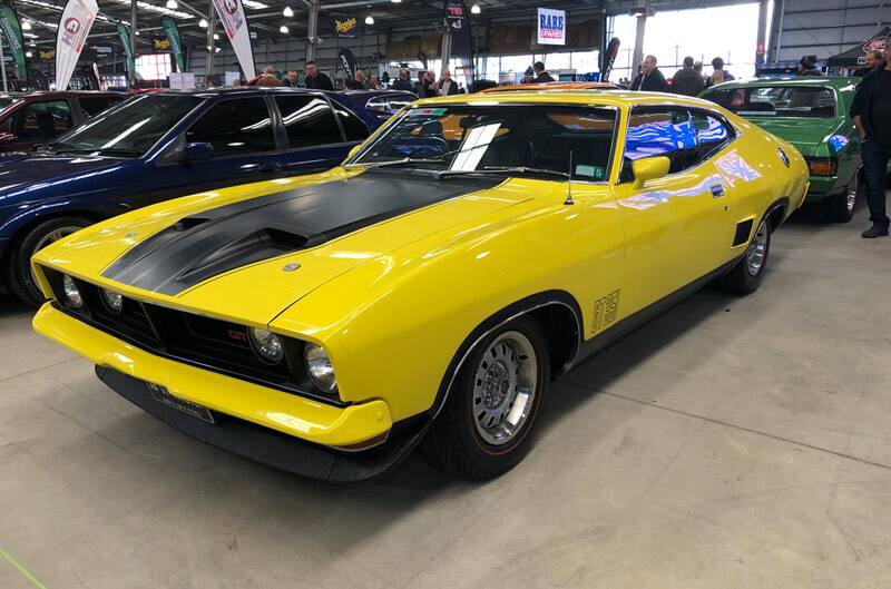 Front profile of yellow GT with black stripe on hood on display at car show