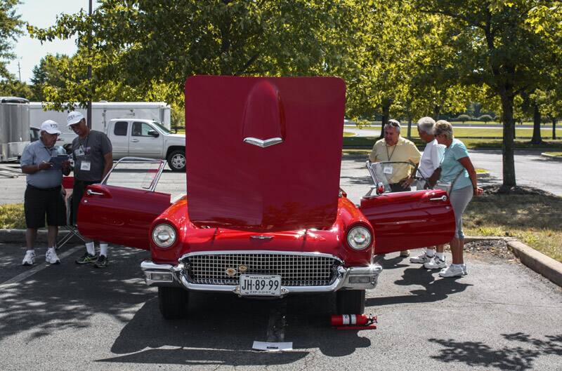 Front of red Thunderbird parked with hood and doors open and people looking inside