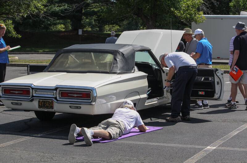 Rear of white Thunderbird droptop with people looking under the hood and inside the car