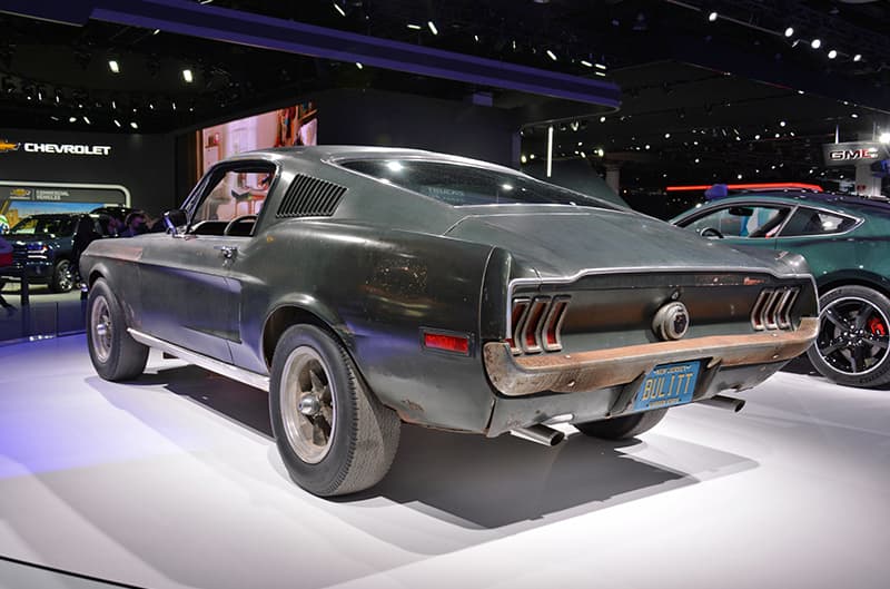 Rear profile of green Mustang Bullitt with rusted bumper on display at car show