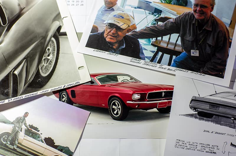 Various pictures and sketches on a desk surrounding a picture of a red Mustang