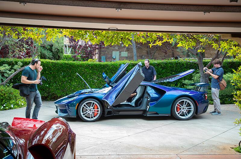 Profile of Mystichrome GT parked on driveway with doors hood and trunk open with men observing it