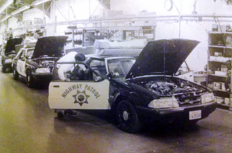 Black and white photo of various black highway patrol Mustang LXs in line in a garage being looked at