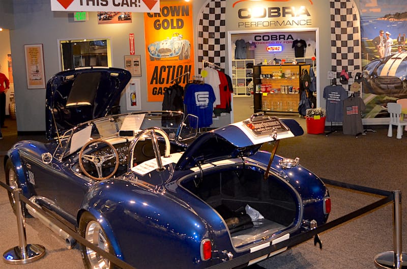 Rear of blue Shelby Cobra droptop with roof down and hood and trunk open on display in museum
