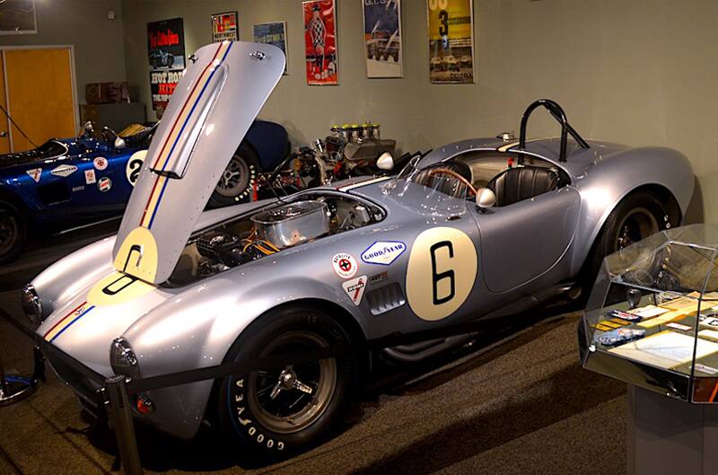 Front profile of blue Shelby Cobra droptop with roof down and hood open on display in museum