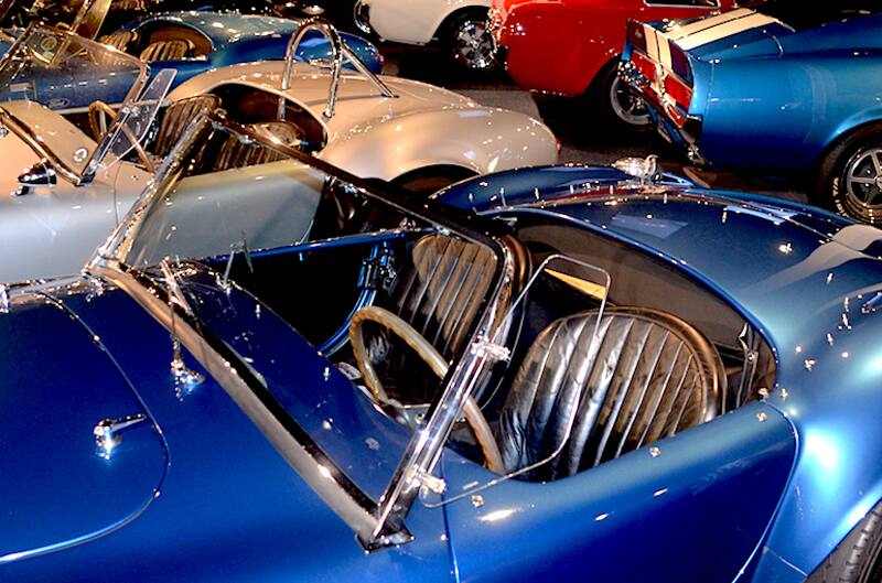 Close up of blue Shelby Cobra with roof down parked close to other Shelby Cobras