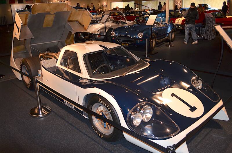 Front profile of a blue and white Shelby Cobra with trunk hood off on display in museum