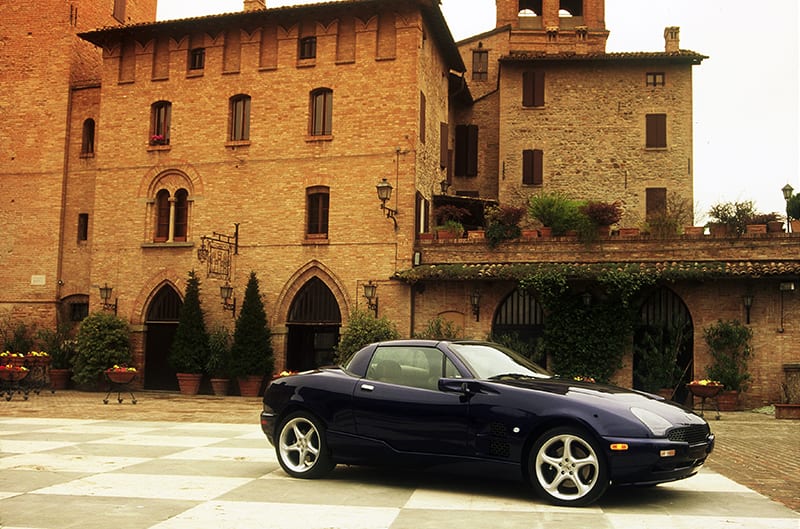 Profile of black Mangusta Qvale in front of mansion