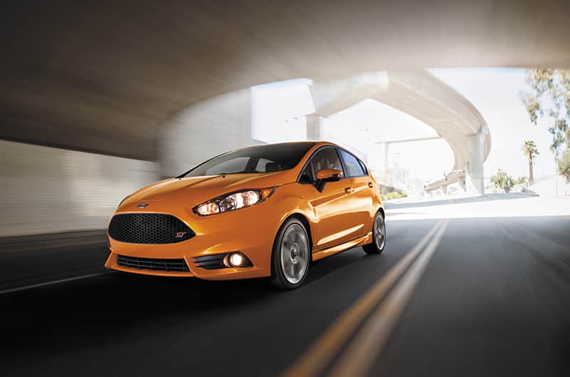  Front profile of orange Fiesta driving on road under a bridge