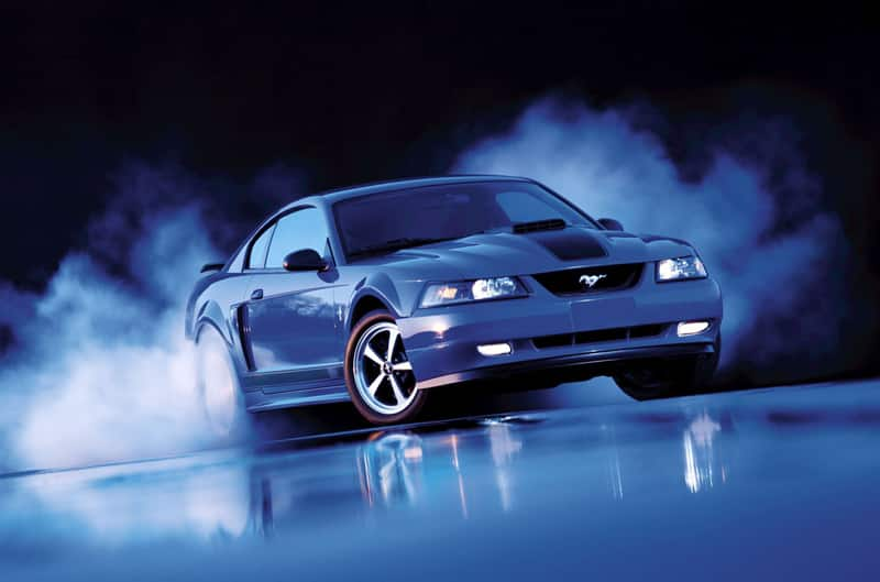 Front of a blue Mustang Mach 1 doing a burnout in a dark garage