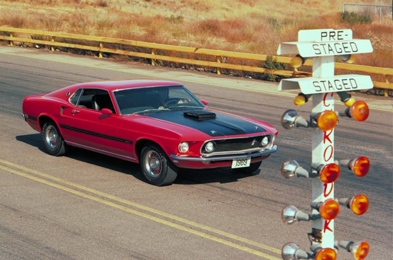 Profile of red Mustang Mach 1 with black hood driving on the road