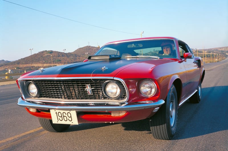 Front of the red Mustang Mach 1 with black hood driving on the road