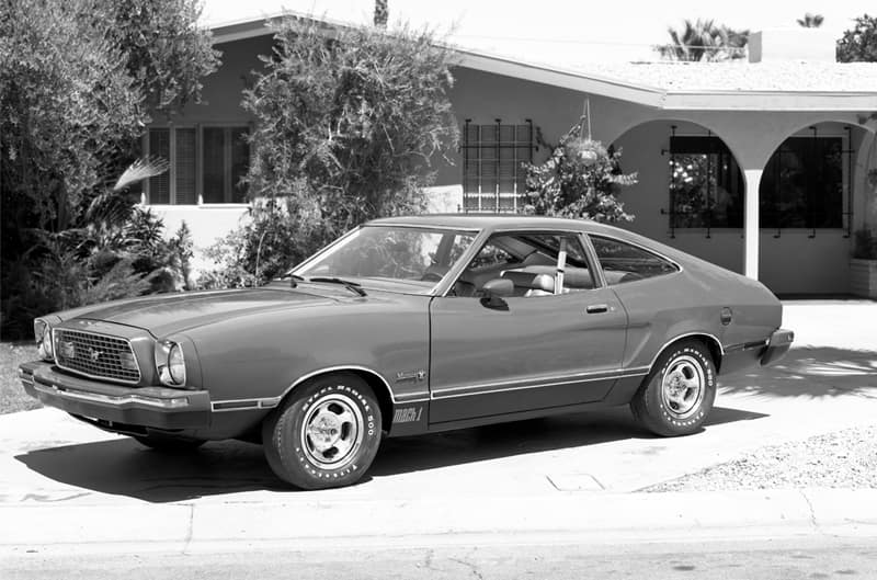 Black and white photo of a profile of Mustang Mach 1 in front of a house