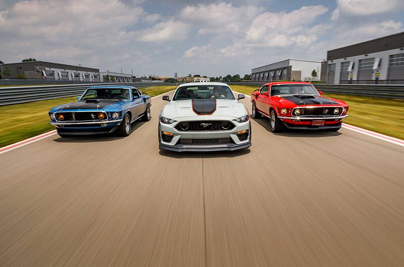 Fronts of a blue white and red Mustang Mach 1s driving on the road