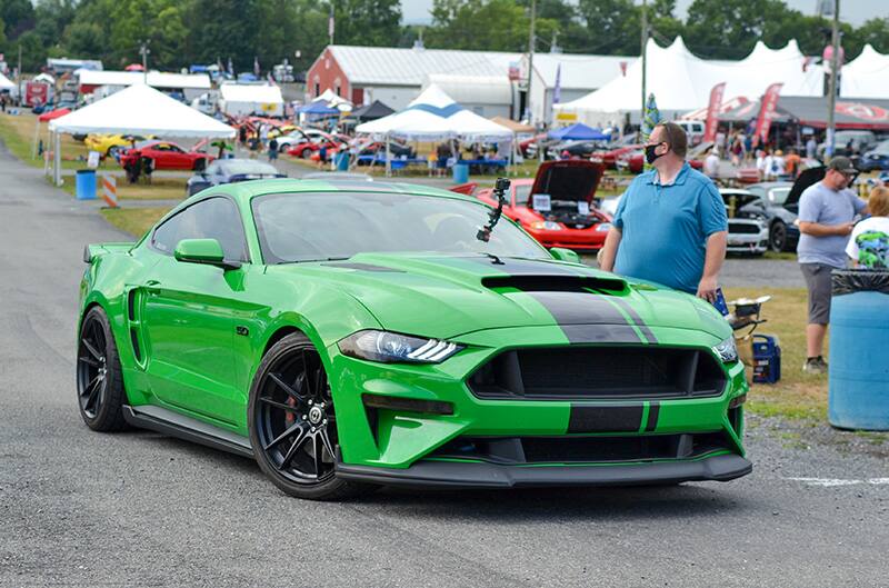 Front of a green Mustang with black stripe and wheels turned on the pavement