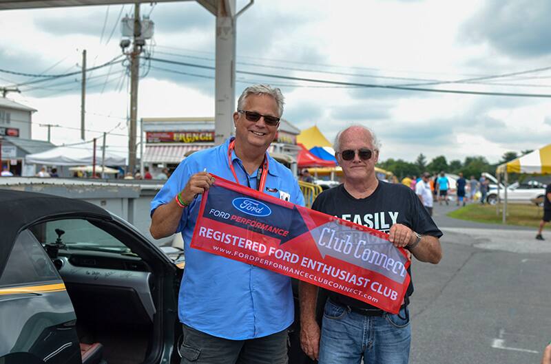 Two men holding up the Ford Performance Club Connect banner in the parking lot