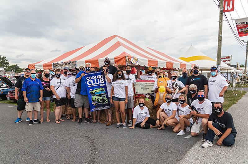 Group of people posing with the Coolest Club poster in front of tents