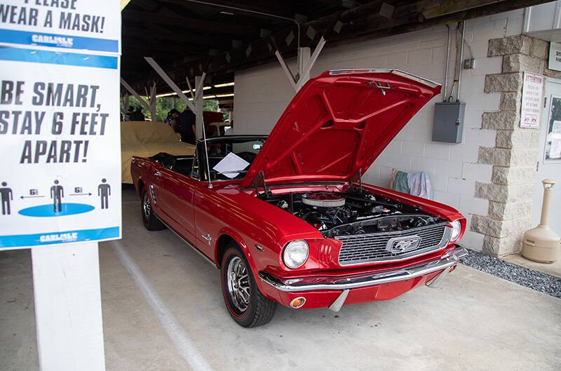 Front of a red Mustang droptop with roof down and hood open parked under a pavilion