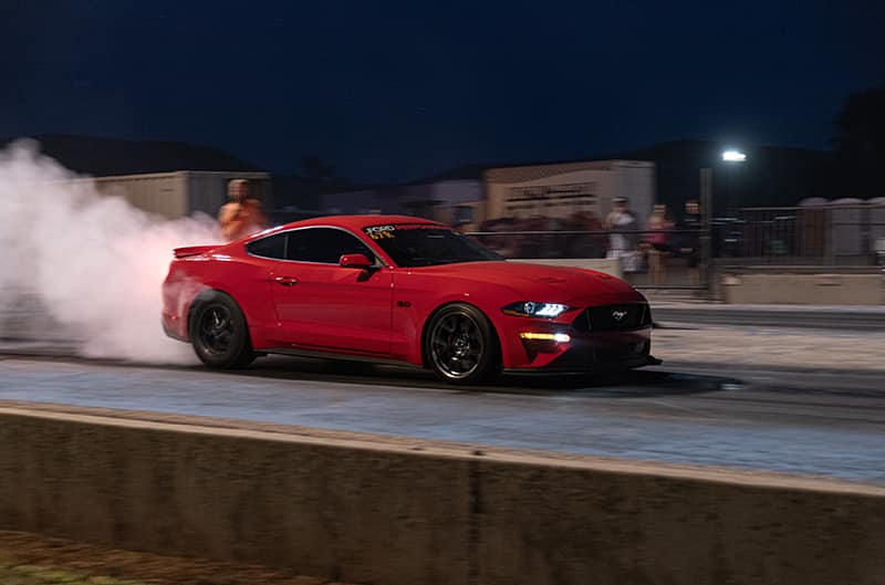 Red 2019 mustang doing a burnout at the drag strip
