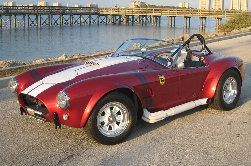 Red FIA Cobra with white stripes in front of lake with pier