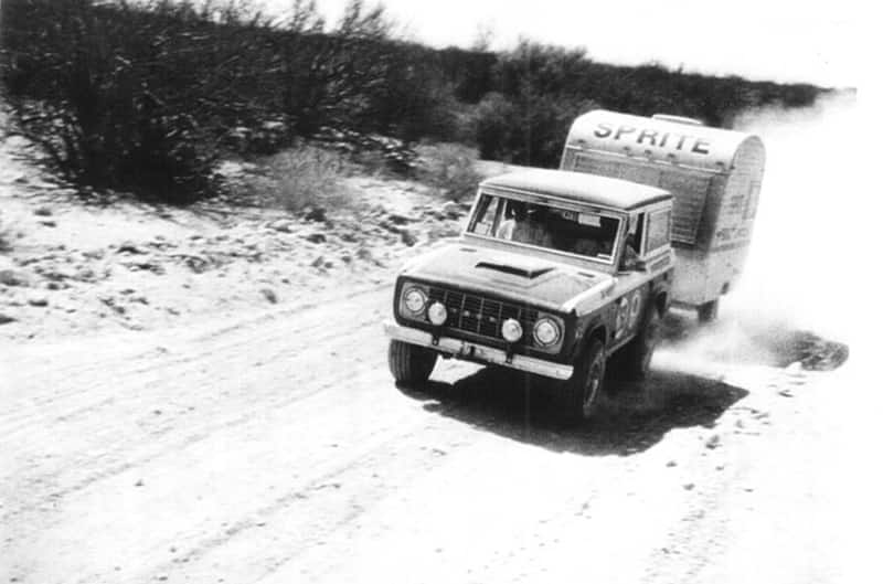 White and Black photo of Stroppe Bronco pulling sprite trailer off-road