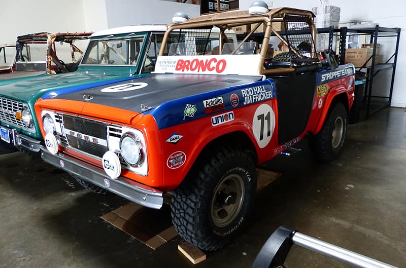 This 1973 Ford Bronco has been modified in the style of a Bill Stroppe Baja  Bronco with orange, white, and blue paint over a white vinyl…