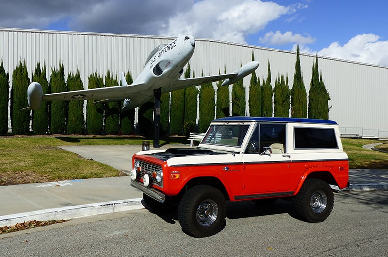 Orange and white Stroppe Bronco outside with plane in background