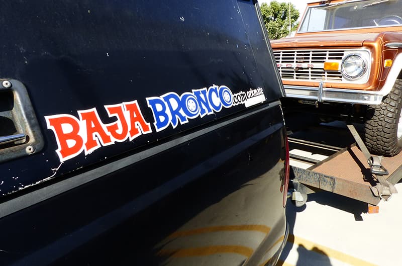 Brown 1960s bronco on trailer being pulled by truck with Baja Bronco sticker on cab