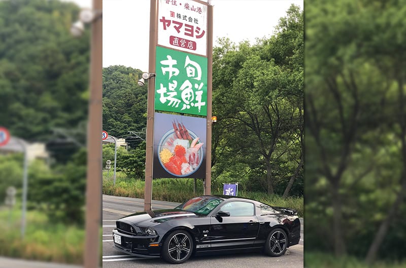 Mustang parked under sign with Japanese writing