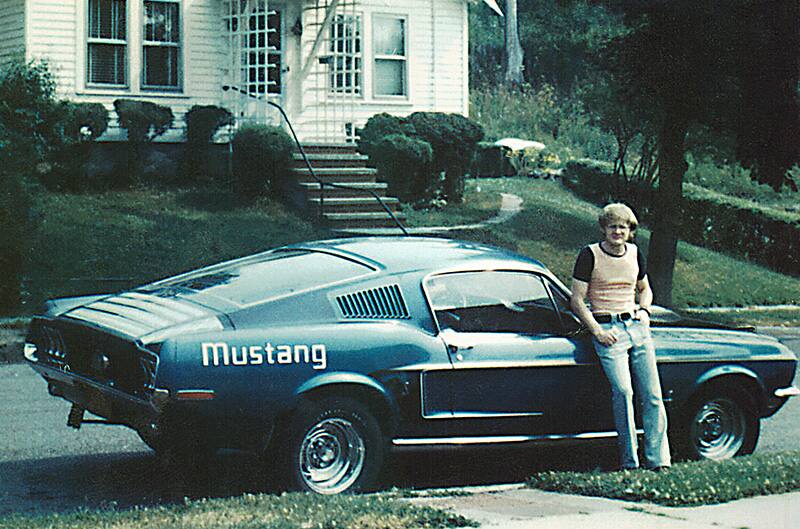 1st mustang sitting in street with man leaning against passenger door