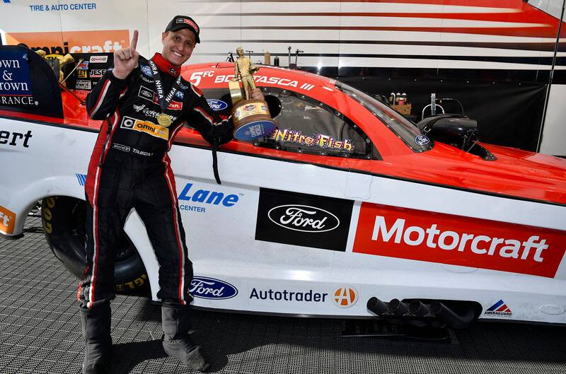 Bob Tasca III holding trophy up next to Mustang funny car