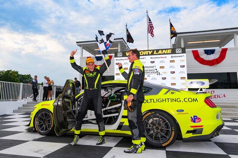 Trent Hindman and Alan Brynjolfsson celebrating in victoy lane with their yellow Ford Mustang GT4