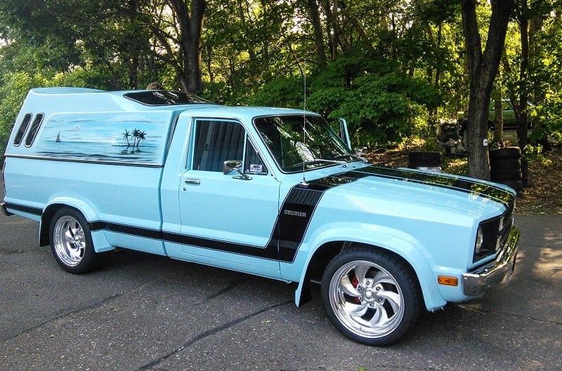 Passenger side view of blue 1978 Ford Courier pickup on street in front of trees