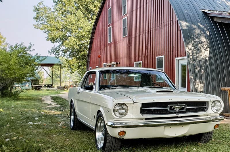 Wimbledon White 1965 Mustang GT parked next to a barn