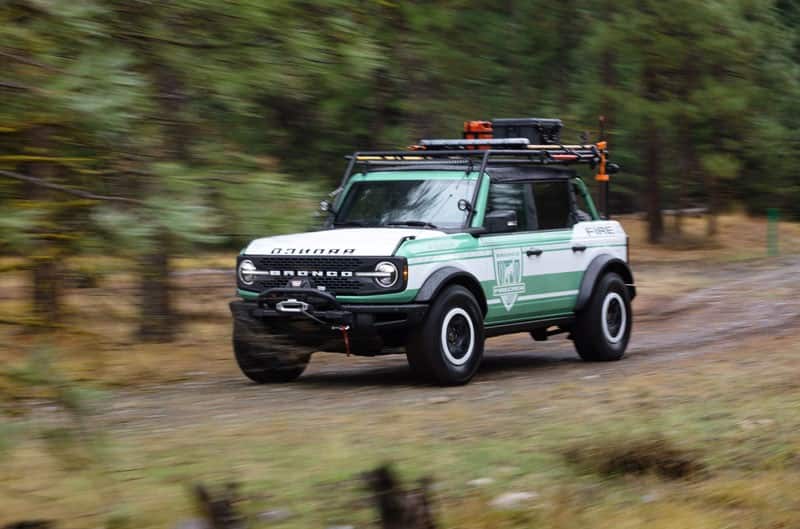 Green and white Bronco driving through the woods