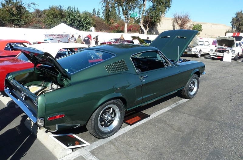 Rear profile of green Mustang with trunk open and hood up in parking lot with other Fords 