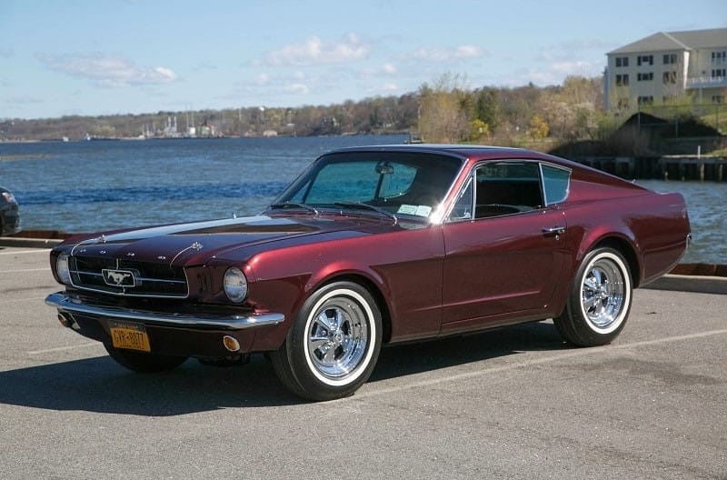 Red Mustang in parking lot in front of water 