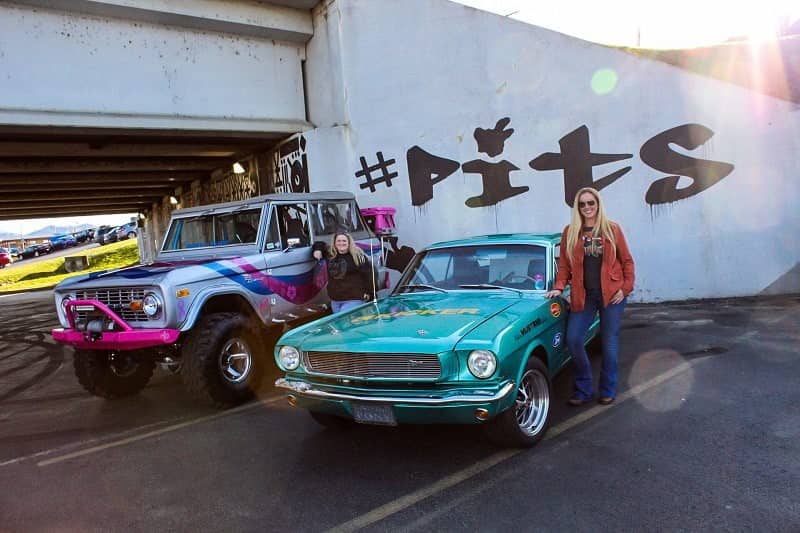 Courtney Barber next to teal Mustang and friend next to her gray pink and blue Bronco