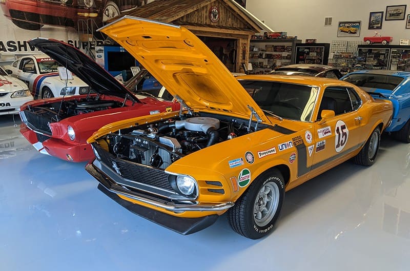 Two classic Mustangs parked in a garage with their hoods up