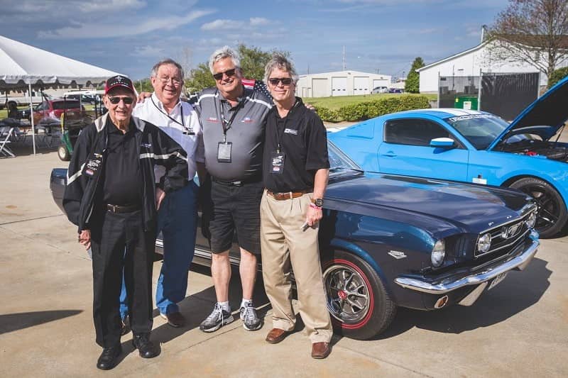 A group of men standing in front of a classic blue Mustang