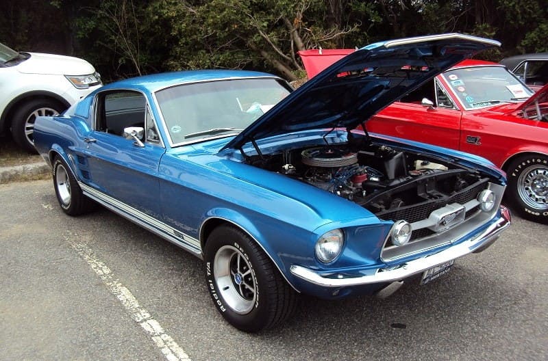 A front side view of a classic Ford Mustang on display with the hood up 