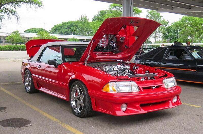 A classic red Ford Mustang on display with the hood and trunk open 