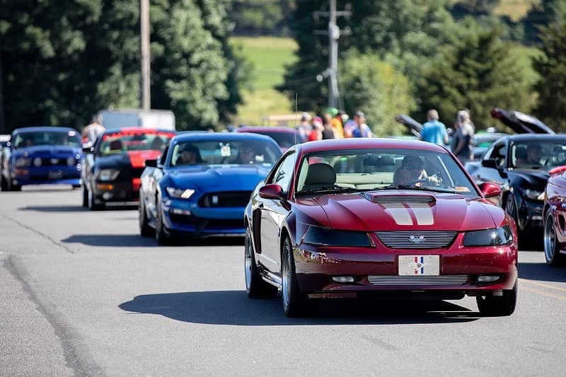 A lineup of a variety of Ford Mustangs driving down the road 