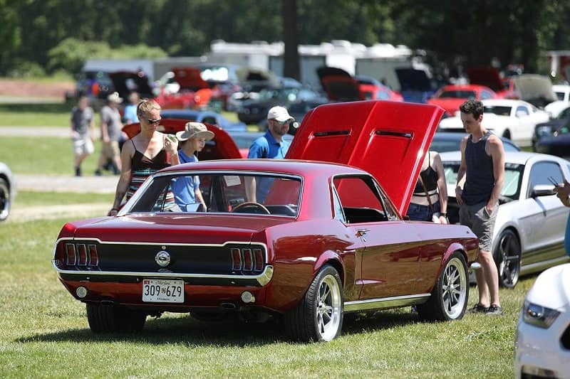 A rear side view of people looking under the hood of a classic red Ford Mustang 