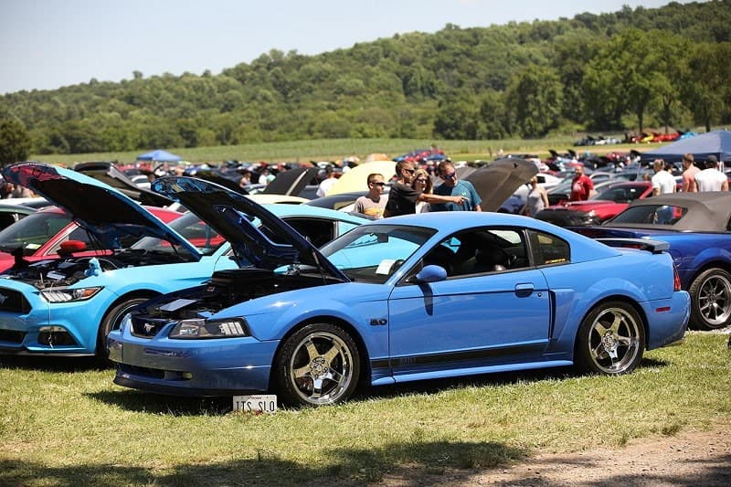 A side view of a blue Ford Mustang on display with the hood up 
