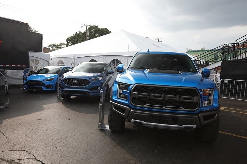 A front end photo of a blue Ford Raptor, Ford Edge S,  and Focus RS