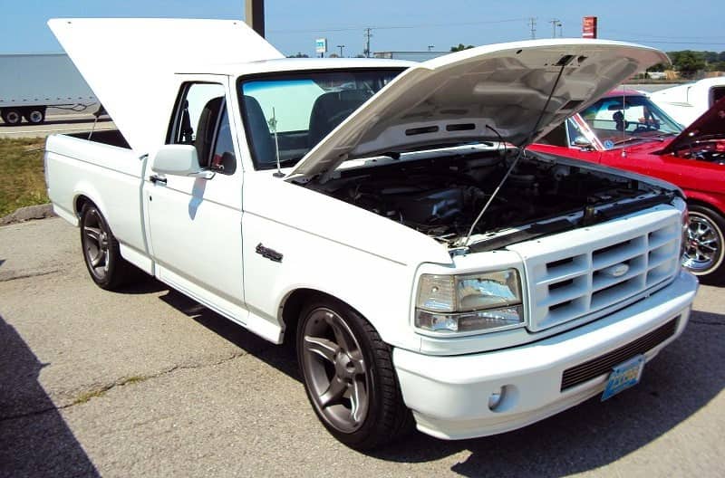 A front side view of a white truck on display with the tailgate and hood open 