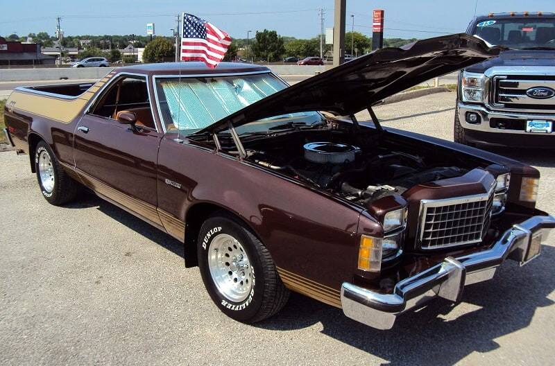 A front side view of a classic vehicle on display with the hood up 
