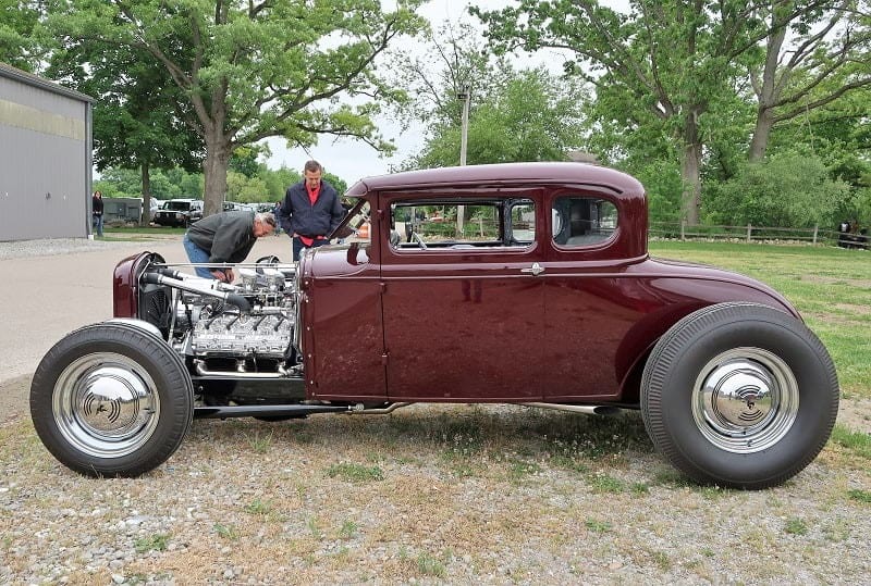 A side view of a couple people admiring the maroon hot rod on display 