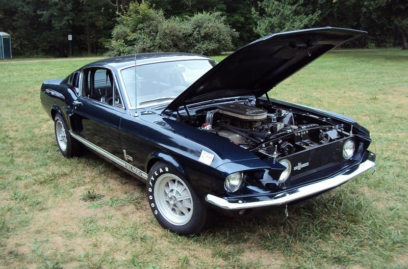 A front side view of a classic Mustang on display with the hood up 
